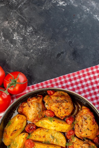 Vertical view of delicious dinner with chickens potatoes greens in saucepan on folded red stripped towel fresh tomatoes on dark color background