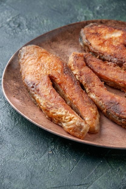 Vertical view of delicious fried fish on a brown plate on mix colors table with free space