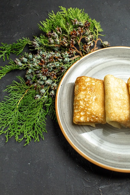 Free Photo vertical view of delicious meat-filled pancakes on a white plate and conifer cone on black background half shot photo