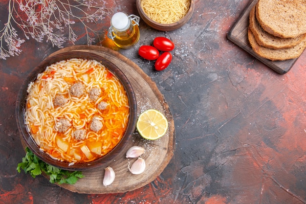 Vertical view of delicious noodle soup with chicken on wooden tary greens oil bottle garlic lemon tomatoes and bread slices on dark background