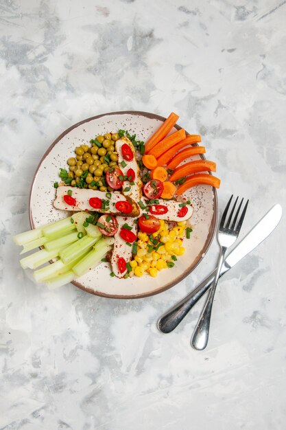 Vertical view of delicious salad with various ingredients on a plate and cutlery set on white surface