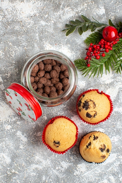 Vertical view of delicious small cupcakes and chocolate in a glass pot and fir branches on ice surface