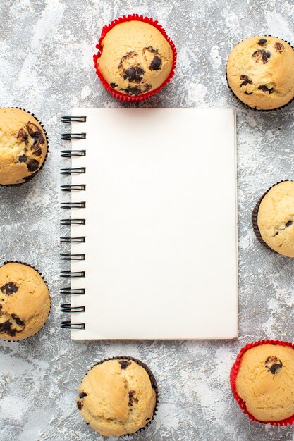 Vertical view of delicious small cupcakes with chocolate around closed notebook on ice surface