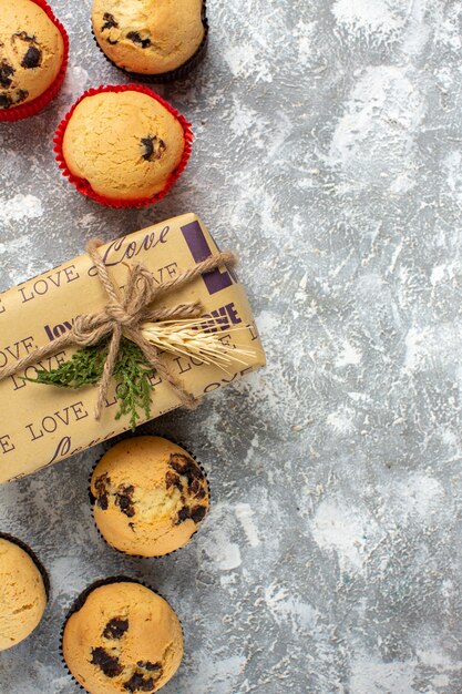 Vertical view of delicious small cupcakes with chocolate and fir branches next to gift on ice surface