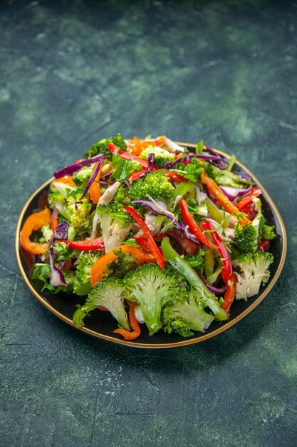 Vertical view of delicious vegan salad in a plate with various fresh vegetables on dark background