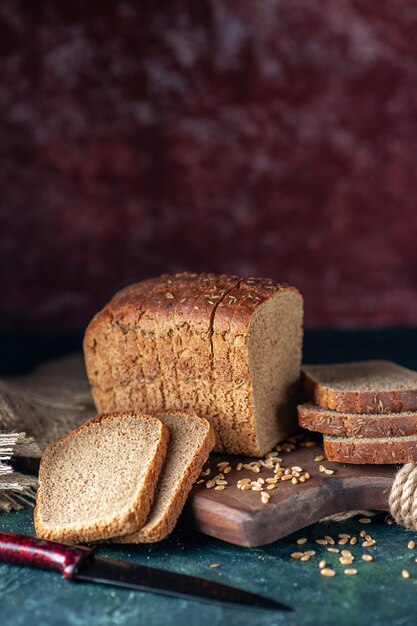 Vertical view of dietary black bread wheats on wooden cutting board knife flower brown towel on mixed colors background