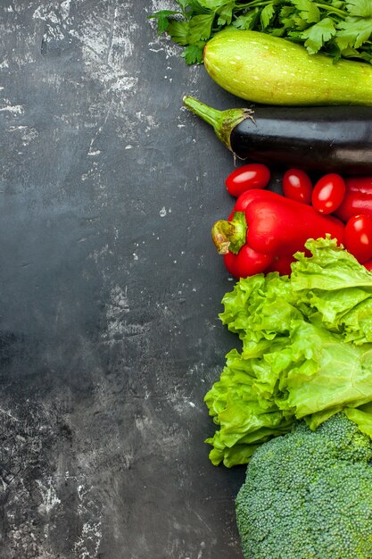 Vertical view of dinner preparation with fresh vegetables and green on the left side on dark background