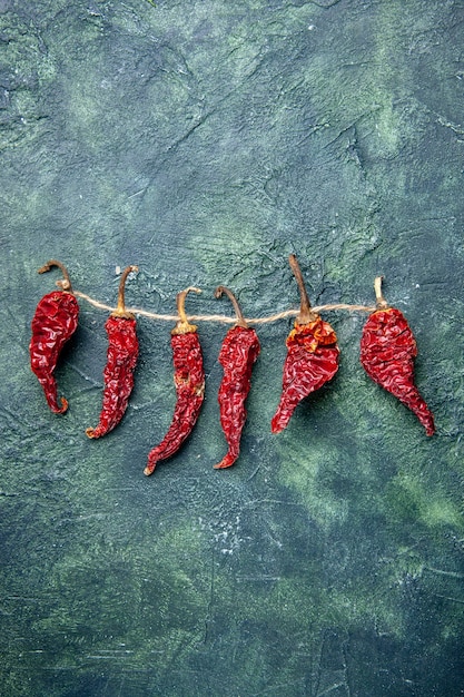 Free Photo vertical view of dried red peppers tied up with rope on green black mixed colors background