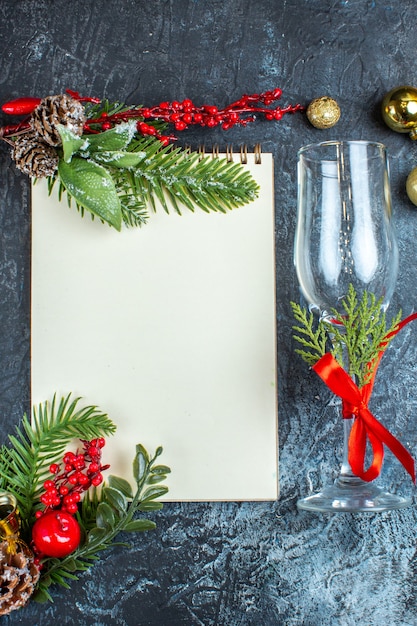 Vertical view of fallen glass goblet with red ribbon and decoration accessories next to notebook on dark background