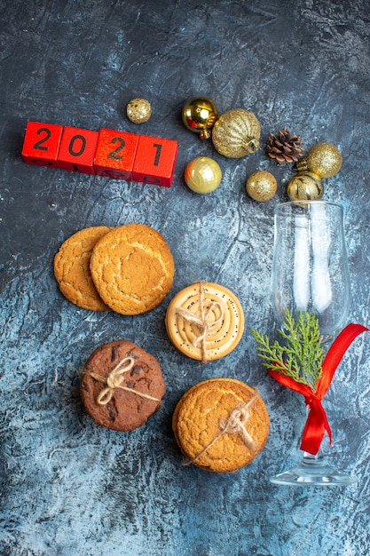 Free photo vertical view of fallen glass goblet with red ribbon and decoration accessories next to stacked cookies numbers on dark background