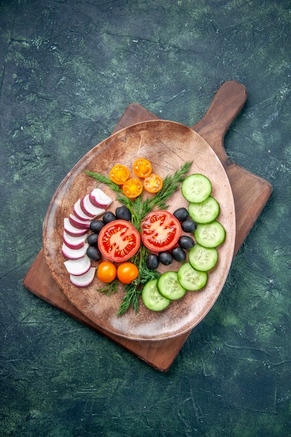 Free photo vertical view of fresh chopped vegetables in a brown plate on wooden cutting board on mixed colors background