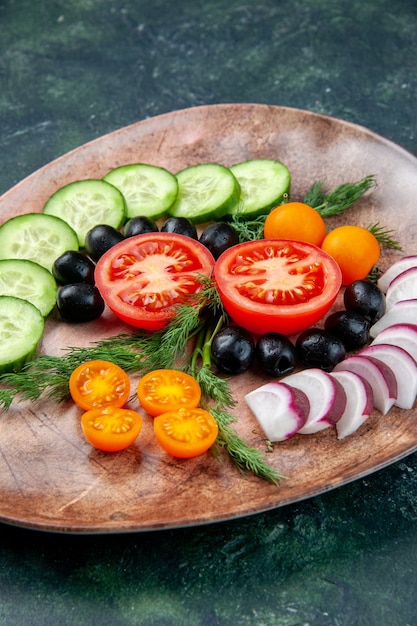 Free photo vertical view of fresh chopped vegetables olives kumquats in a brown plate on green black mixed colors background