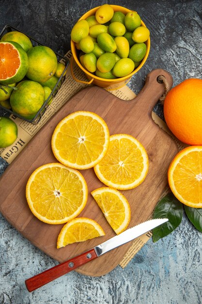 Vertical view of fresh citrus fruits with knife on wooden cutting board on newspaper on gray background