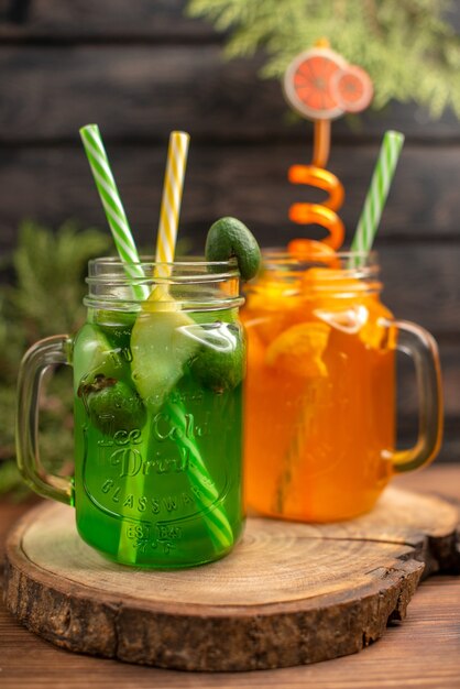 Vertical view of fresh fruit juices in a glass served with tubes on a wooden cutting board on a brown table