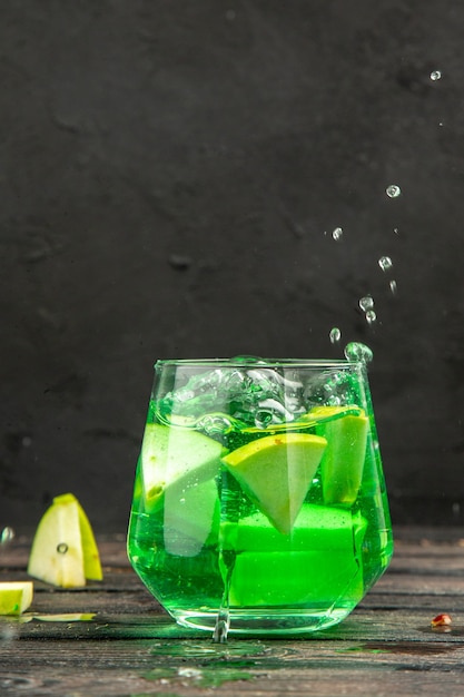 Vertical view of fresh natural delicious juice in a glass served with apple limes on black background