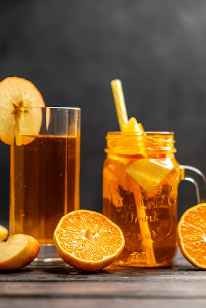 Vertical view of fresh natural delicious juice in two glasses hand putting fruit limes with tube in it on black background