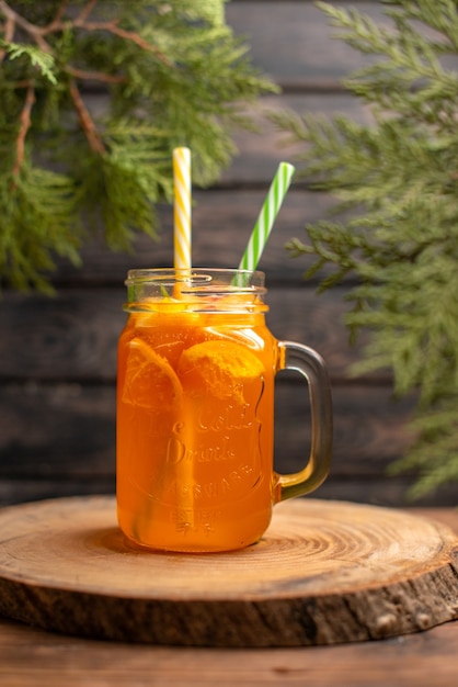 Vertical view of fresh orange juice in a glass with tube on a wooden tray on brown background