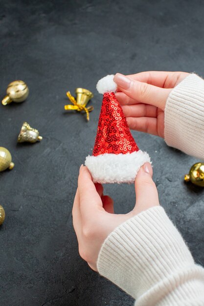 Vertical view of hand holding santa claus hat and decoration accessories on dark background