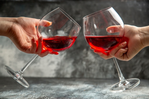 Vertical view of hands holding glasses of dry red wine on gray background