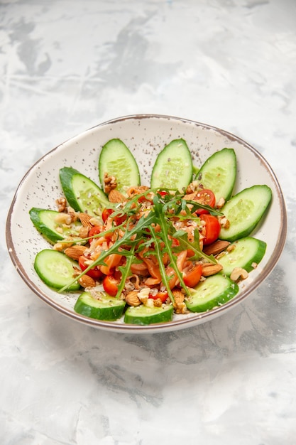 Free photo vertical view of homemade healthy delicious vegan salad decorated with chopped cucumbers in a bowl on stained white surface