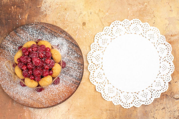 Free photo vertical view of homemade soft cake with fruits and napkin on wooden cutting board on mixed color table