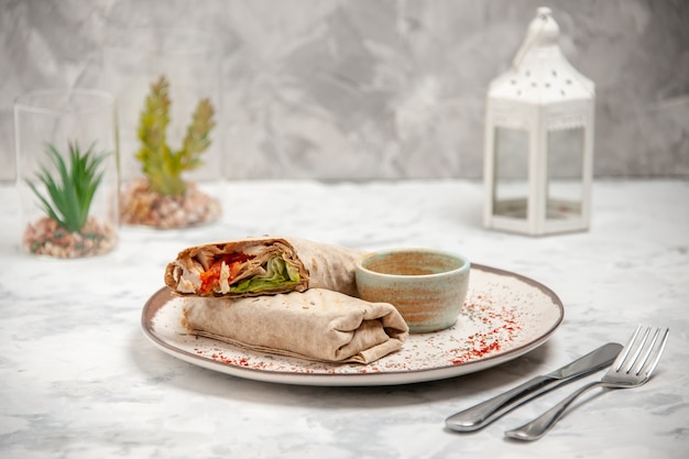 Vertical view of lavash wrap and yogurt in a small bowl on a plate and toy house cutlery set on stained white surface