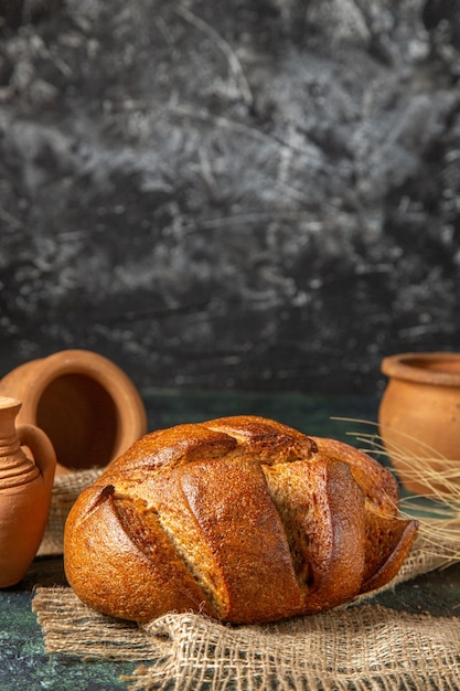 Vertical view of a loaf of dietary black bread on brown towel and potteries on dark colors surface