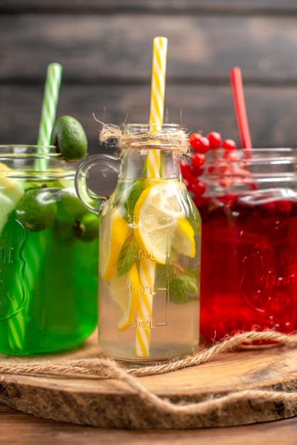 Vertical view of natural organic fuit juices in bottles served with tubes on a wooden cutting board