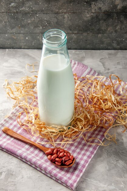 Vertical view of open glass bottle filled with milk and bean in spoon on purple stripped towel