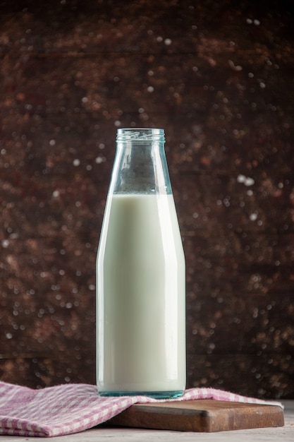 Vertical view of open glass bottle filled with milk on purple stripped towel on wooden cutting board