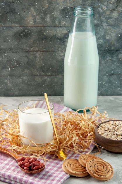 Vertical view of open glass cup bottle filled with milk and bean in spoon cookies oats on purple stripped towel