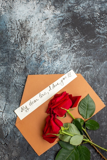 Free photo vertical view of red roses and envelope with love letter on icy dark background