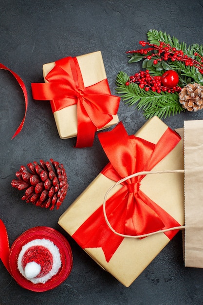 Vertical view of a roll of red ribbon conifer cones and gift fir branches on dark background