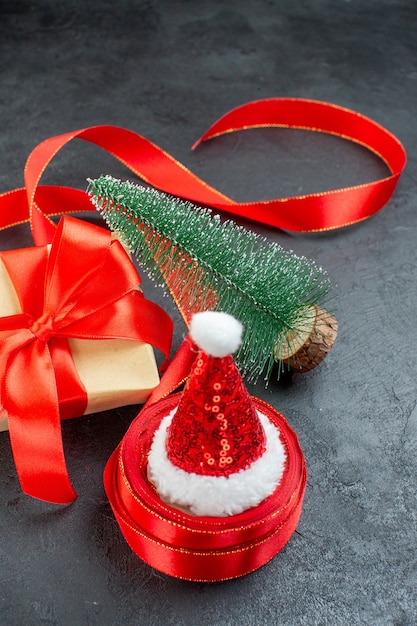 Free Photo vertical view of santa claus hat on a roll of ribbon and beautiful gift christmas tree on dark background