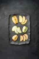 Free photo vertical view of several types of sliced fresh apples on a black tray on a dark background