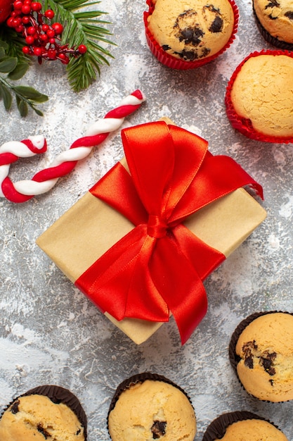 Vertical view of small cupcakes Christmas gifts with red ribbon and candy fir branches on ice table