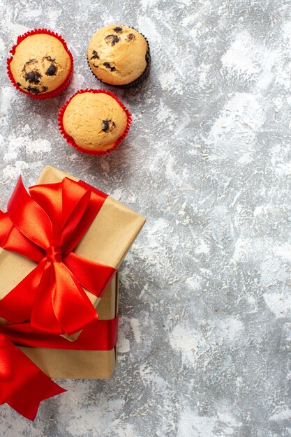 Vertical view of small cupcakes Christmas gifts with red ribbon on ice surface