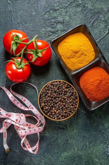 Free Photo vertical view of spice bowls fulfilled with red pepper and yellow ginger meter fresh tomatoes with stem on mix colors surface