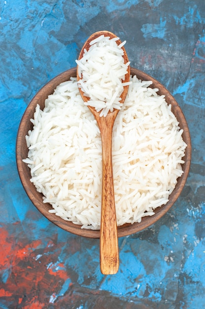 Vertical view of tasty rice meal in a brown small pot and wooden spoon on blue background