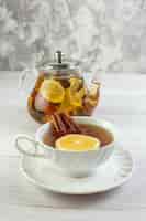 Free photo vertical view of tea time with mixed herbal tea with lemon in a glass pot and a cup on white table