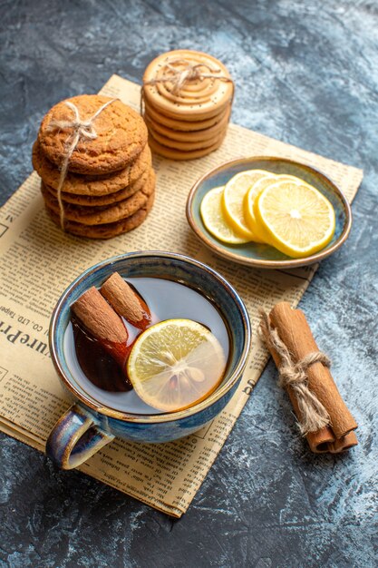 Vertical view of tea time with stacked delicious cookies cinnamon lemon on an old newspaper on dark background