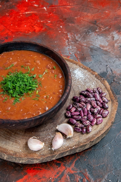 Free photo vertical view of tomato soup beans garlic on wooden cutting board on mix color background