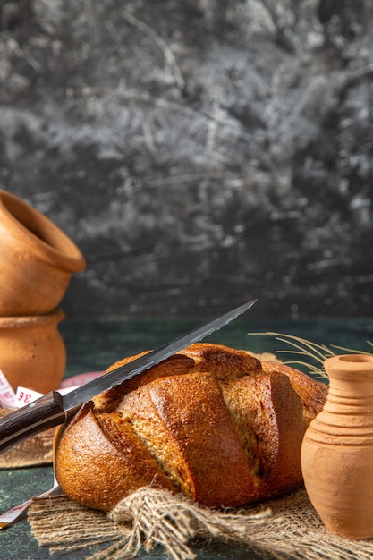 Vertical view of whole black bread on brown towel potteries on dark colors surface