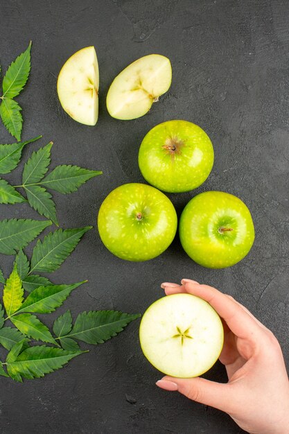 Vertical view of whole and chopped fresh green apples and mint on black background