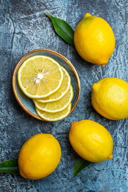 Vertical view of whole and cut fresh lemons with leaves on the left side on dark background