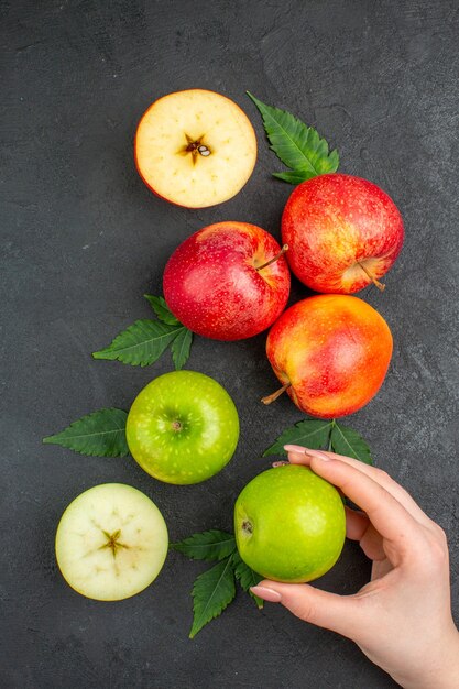 Vertical view of whole and cut fresh natural apples and leaves on black table