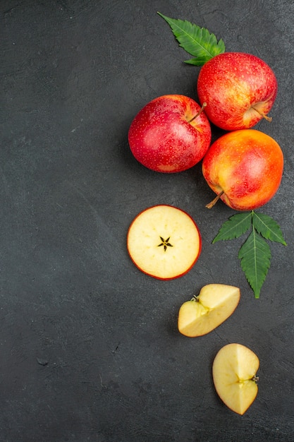 Vertical view of whole and cut fresh natural organic red apples with green leaves on black background