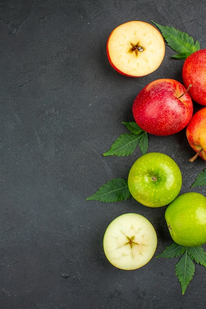 Vertical view of whole and cut fresh red apples and leaves on the left side on black background