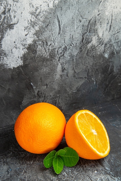 Free photo vertical view of whole and cut in half fresh oranges on gray background