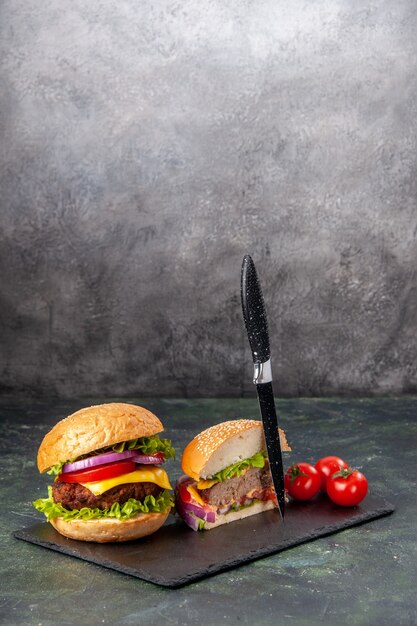 Vertical view of whole cut various tasty sandwiches and tomatoes with stem knife on black tray on dark mix color surface